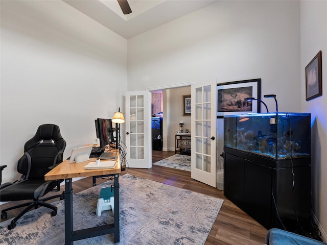 home office with wood finished floors, a towering ceiling, baseboards, a ceiling fan, and french doors