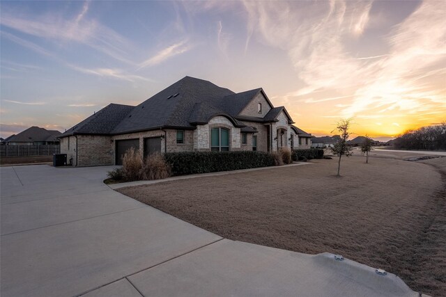 french provincial home featuring a garage, stone siding, brick siding, and driveway