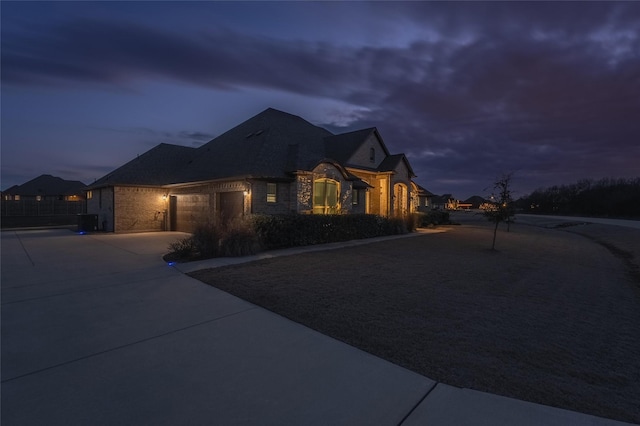 french country inspired facade with a garage, concrete driveway, and stone siding