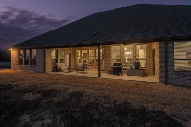 back of property featuring a yard, a shingled roof, a patio, and brick siding