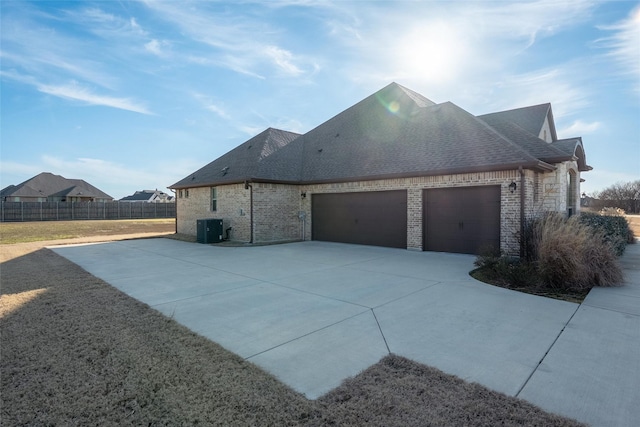 view of side of property with an attached garage, central AC, brick siding, fence, and concrete driveway