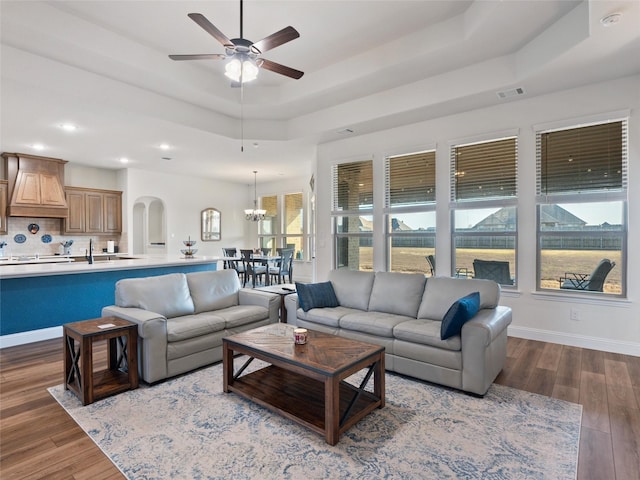 living area featuring baseboards, visible vents, arched walkways, wood finished floors, and a tray ceiling