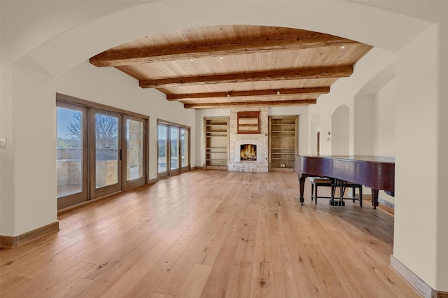 living room featuring light wood finished floors, baseboards, wooden ceiling, a brick fireplace, and beam ceiling