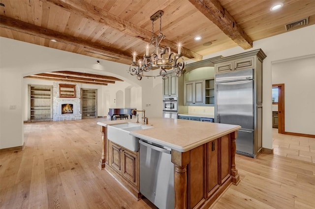 kitchen with visible vents, arched walkways, an island with sink, hanging light fixtures, and stainless steel appliances