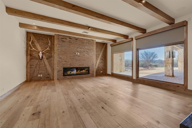 unfurnished living room with a large fireplace, beam ceiling, visible vents, and light wood-style floors