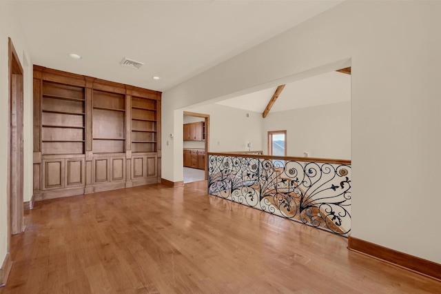 spare room with vaulted ceiling with beams, light wood finished floors, baseboards, and visible vents