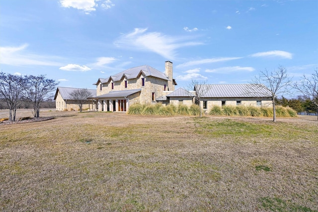 exterior space featuring stone siding, a yard, a chimney, and metal roof