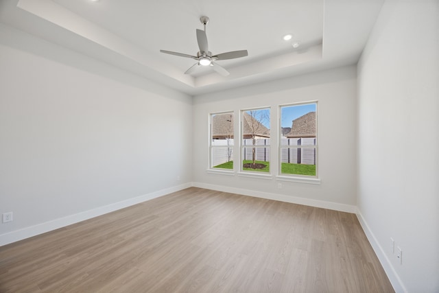 unfurnished room featuring light wood-style floors, a tray ceiling, baseboards, and a ceiling fan