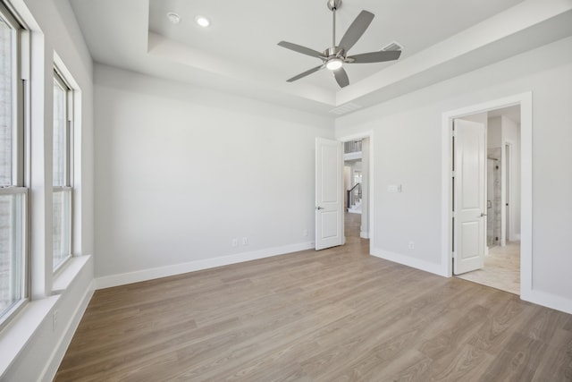 unfurnished bedroom with light wood finished floors, multiple windows, baseboards, and a raised ceiling