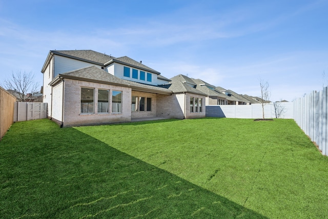 rear view of property with a shingled roof, a fenced backyard, brick siding, and a lawn