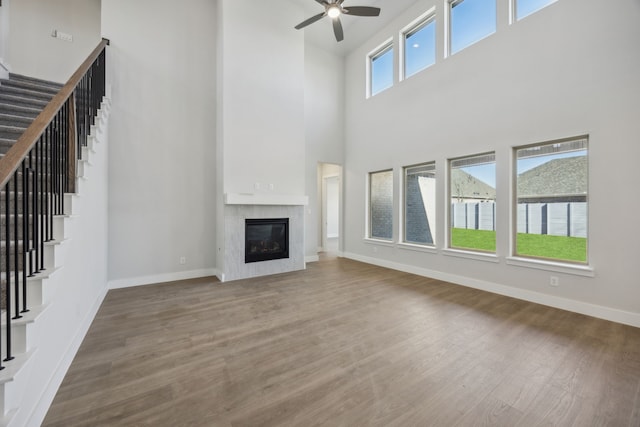 unfurnished living room with stairs, a glass covered fireplace, baseboards, and wood finished floors