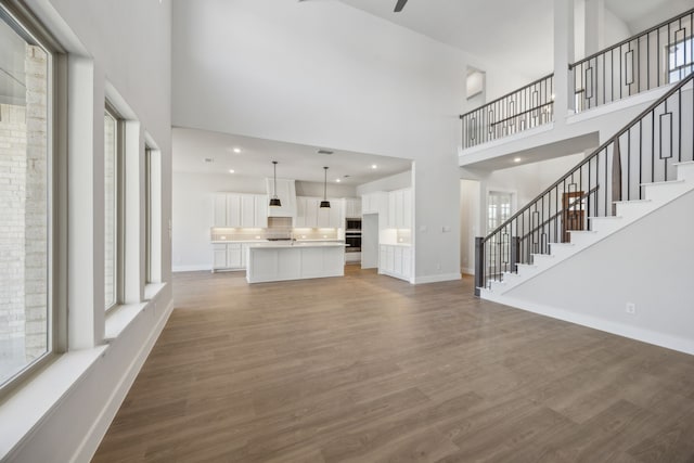 unfurnished living room featuring stairway, wood finished floors, a towering ceiling, and baseboards