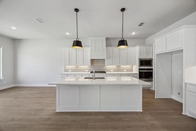 kitchen featuring an island with sink, light countertops, and oven