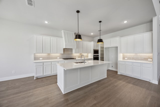 kitchen featuring a kitchen island with sink, white cabinets, light countertops, and a sink