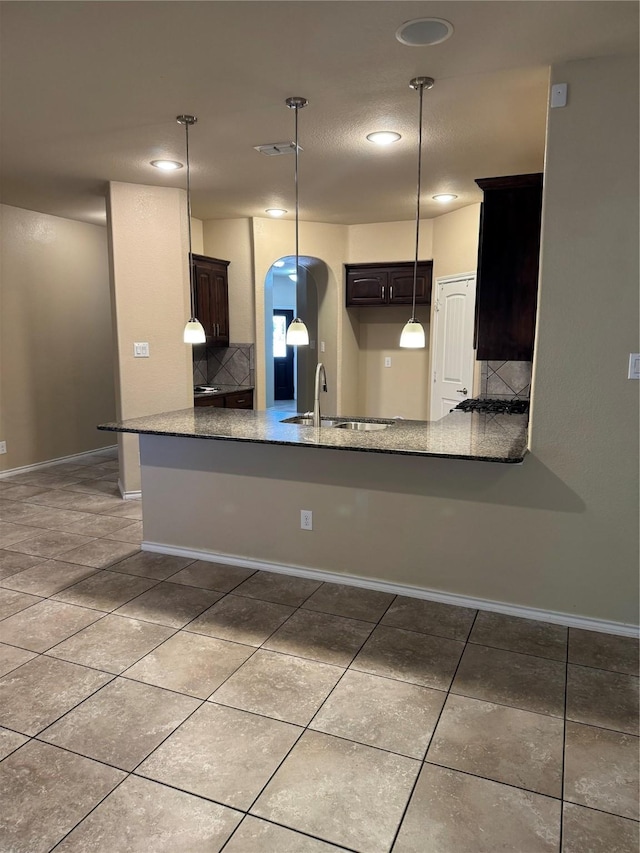 kitchen featuring arched walkways, dark brown cabinetry, a peninsula, and a sink