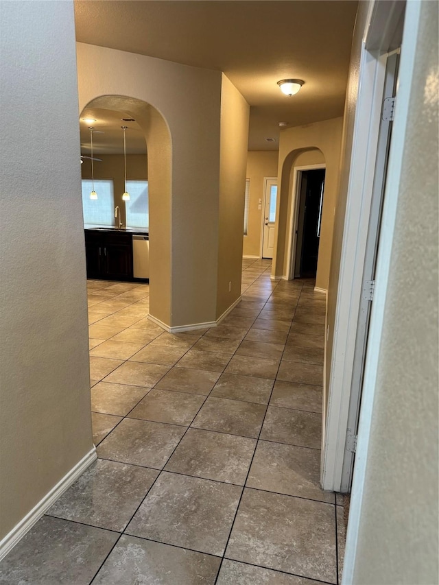 corridor featuring baseboards, arched walkways, and dark tile patterned flooring