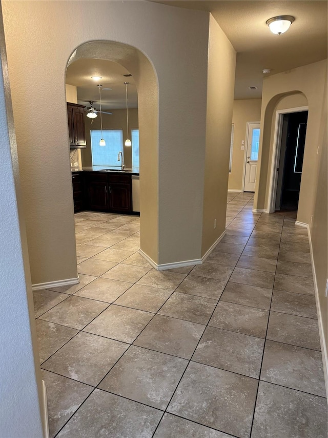 corridor featuring a wealth of natural light, arched walkways, baseboards, tile patterned flooring, and a sink