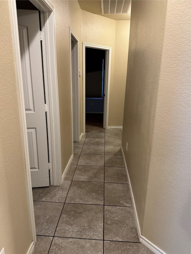 hallway with visible vents, a textured wall, dark tile patterned floors, and baseboards