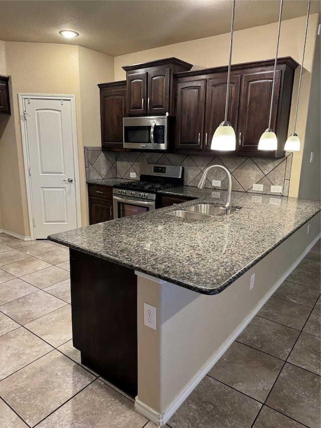 kitchen featuring stainless steel appliances, hanging light fixtures, a sink, dark stone countertops, and a peninsula