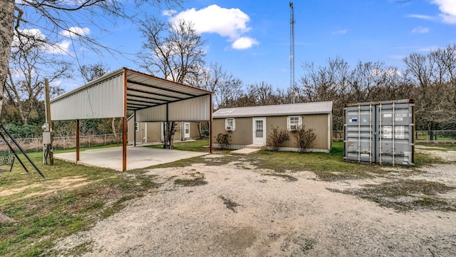 rear view of property featuring dirt driveway, metal roof, fence, an outdoor structure, and a detached carport