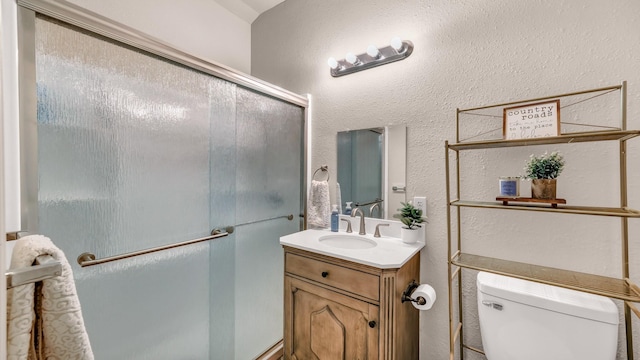 bathroom featuring toilet, a textured wall, a shower with shower door, and vanity