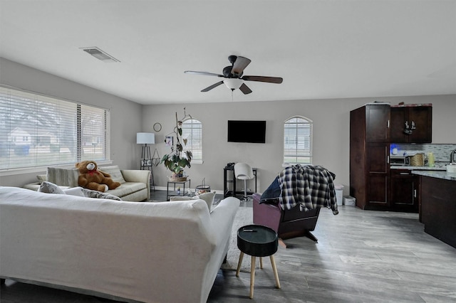 living room with light wood-style floors, a ceiling fan, visible vents, and a wealth of natural light