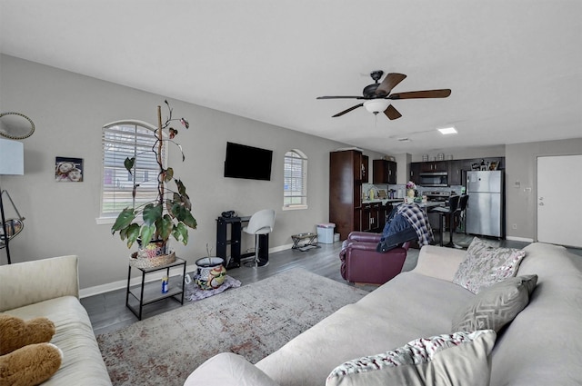 living room with baseboards, a ceiling fan, and dark wood-type flooring