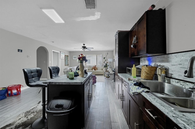 kitchen with arched walkways, a breakfast bar area, a sink, visible vents, and a center island