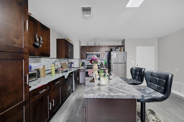 kitchen with a breakfast bar area, stainless steel appliances, a sink, a kitchen island, and visible vents