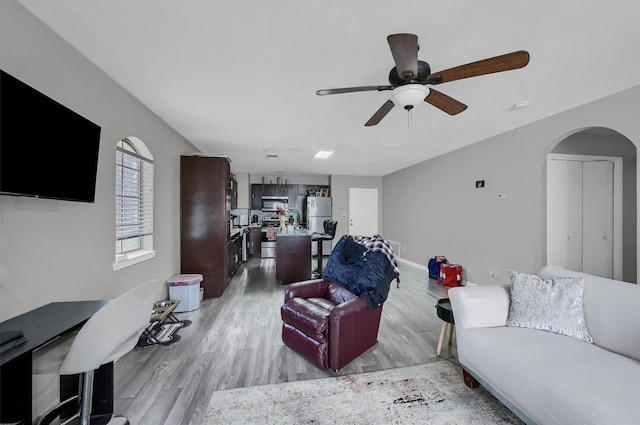 living room featuring light wood finished floors, baseboards, arched walkways, and a ceiling fan