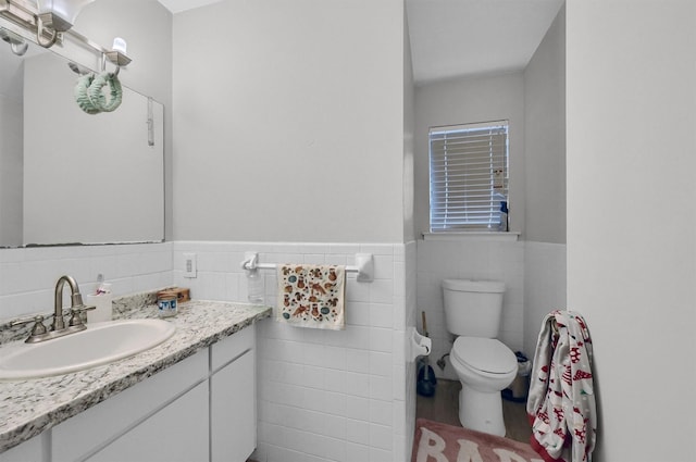 bathroom with tile walls, a wainscoted wall, vanity, and toilet