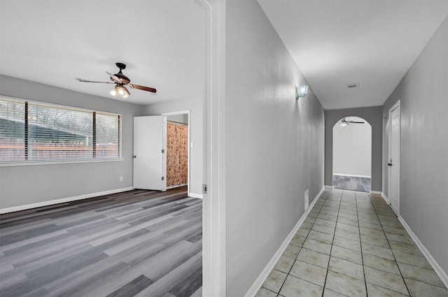 corridor featuring light wood-style floors, arched walkways, and baseboards