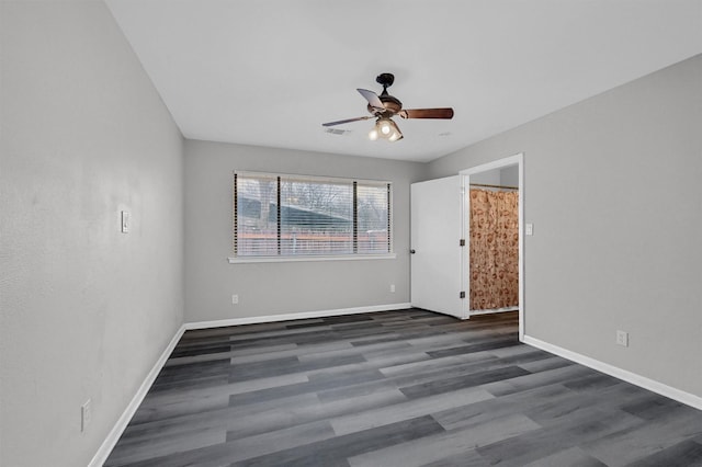 spare room with ceiling fan, visible vents, baseboards, and dark wood finished floors