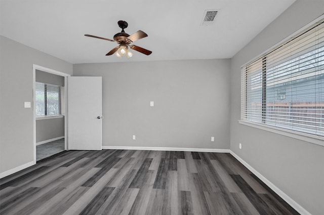 empty room with dark wood-style floors, a ceiling fan, visible vents, and baseboards