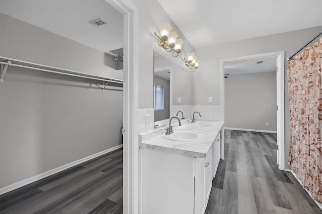 full bath with a walk in closet, wood finished floors, a sink, and double vanity