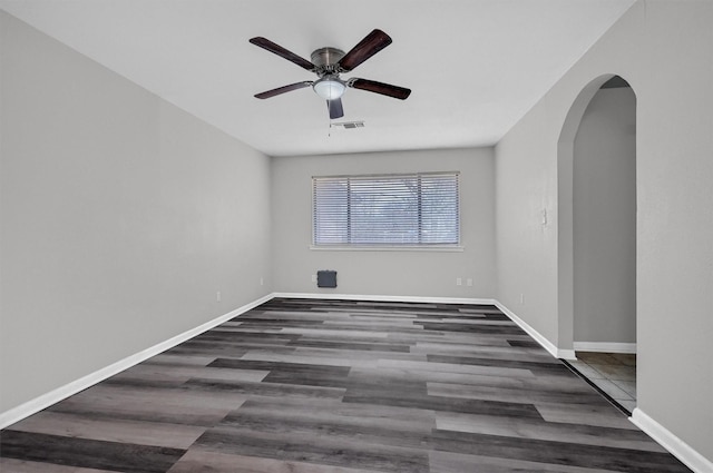 empty room featuring arched walkways, dark wood-style floors, visible vents, and baseboards