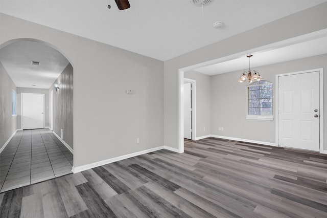 unfurnished room featuring dark wood-style floors, baseboards, arched walkways, and ceiling fan with notable chandelier