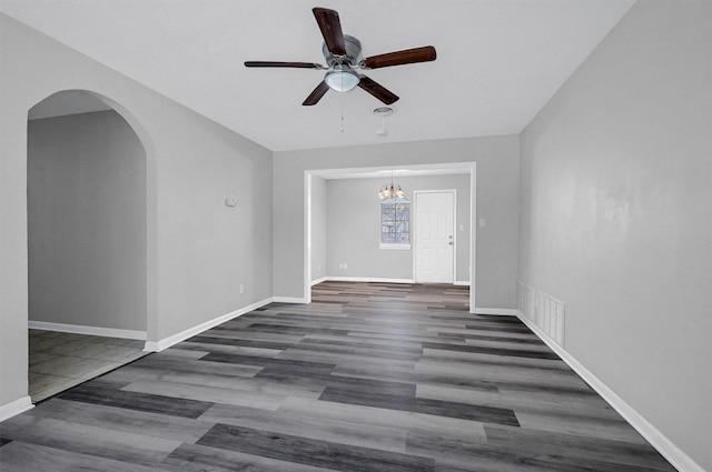 unfurnished room with arched walkways, dark wood finished floors, visible vents, baseboards, and ceiling fan with notable chandelier