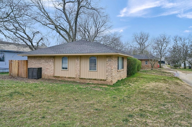 view of side of home with roof with shingles, brick siding, a lawn, and fence