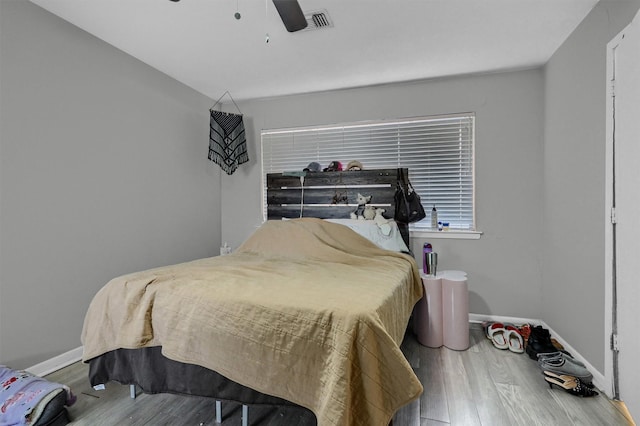 bedroom with a ceiling fan, visible vents, baseboards, and wood finished floors