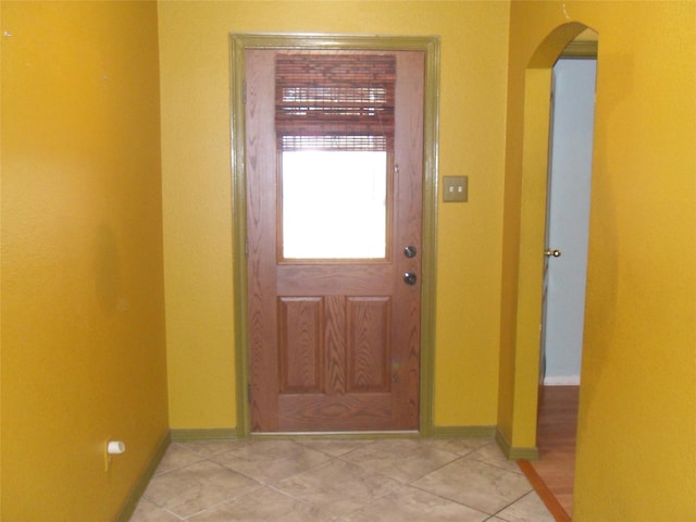 doorway with arched walkways, baseboards, and tile patterned floors