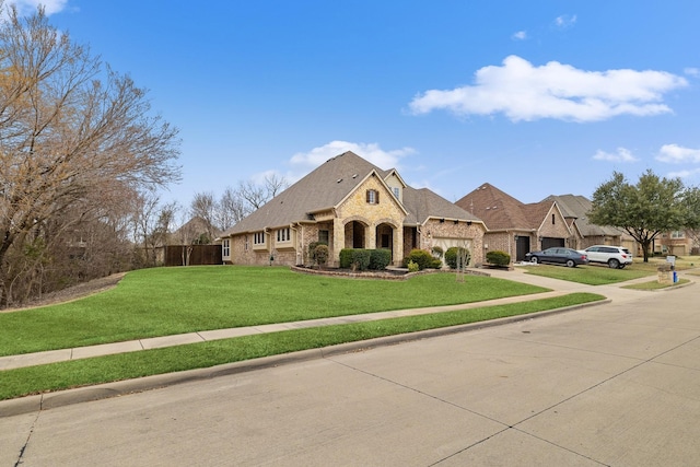 french country style house with a front yard, stone siding, and driveway