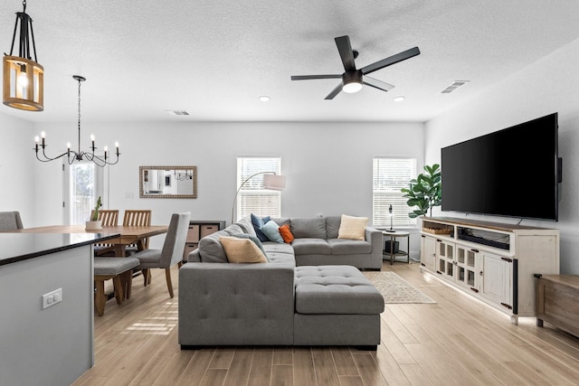 living room featuring light wood-type flooring, visible vents, a textured ceiling, and ceiling fan with notable chandelier