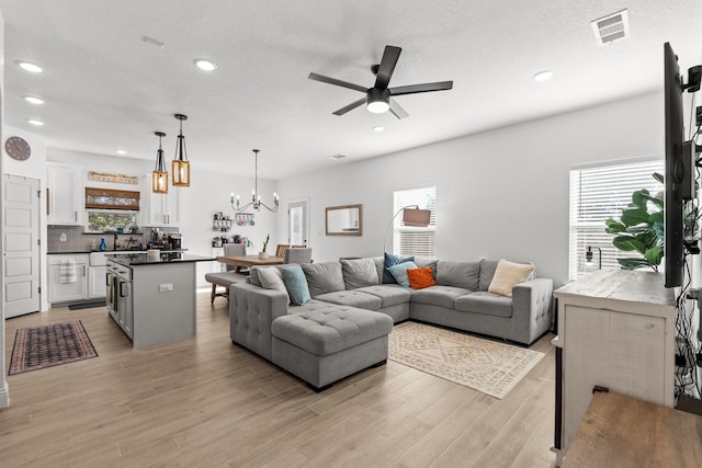 living room with a textured ceiling, recessed lighting, ceiling fan with notable chandelier, visible vents, and light wood finished floors