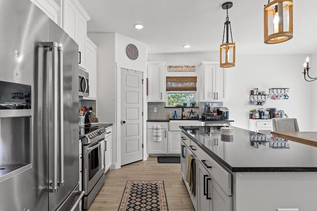 kitchen featuring light wood-style flooring, stainless steel appliances, white cabinetry, tasteful backsplash, and dark countertops