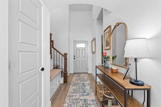 entryway with arched walkways, a textured wall, wood finish floors, baseboards, and stairway