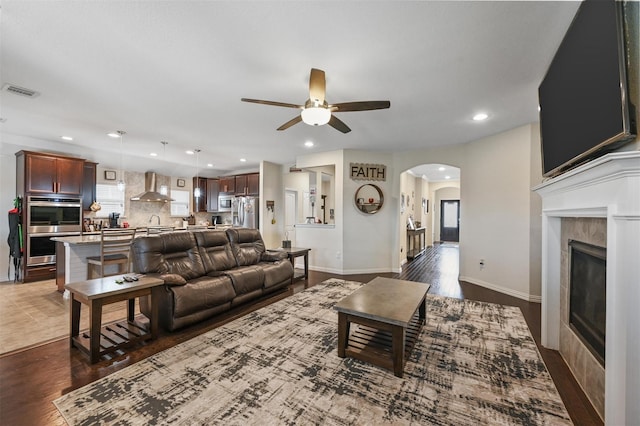 living room featuring arched walkways, dark wood-style flooring, a high end fireplace, visible vents, and a ceiling fan