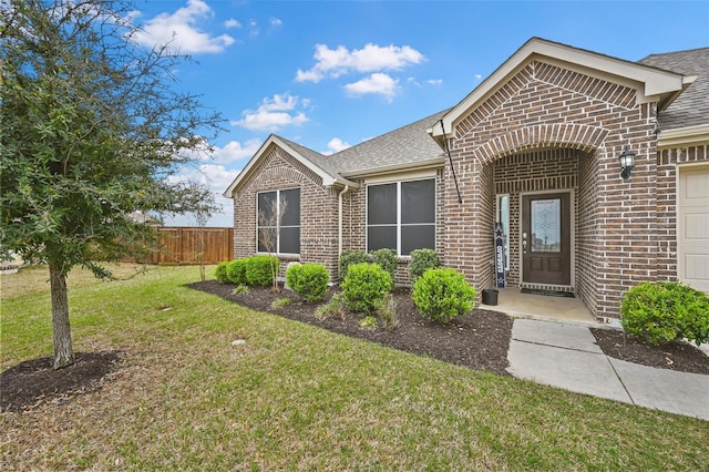 view of front of home with brick siding, a front lawn, a shingled roof, and fence