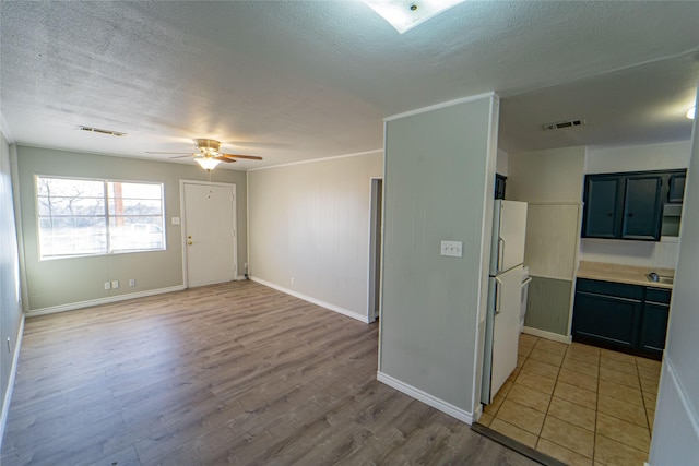 interior space with a ceiling fan, light wood-style flooring, visible vents, and a textured ceiling