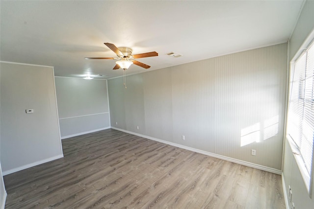 empty room with a ceiling fan, visible vents, baseboards, and wood finished floors